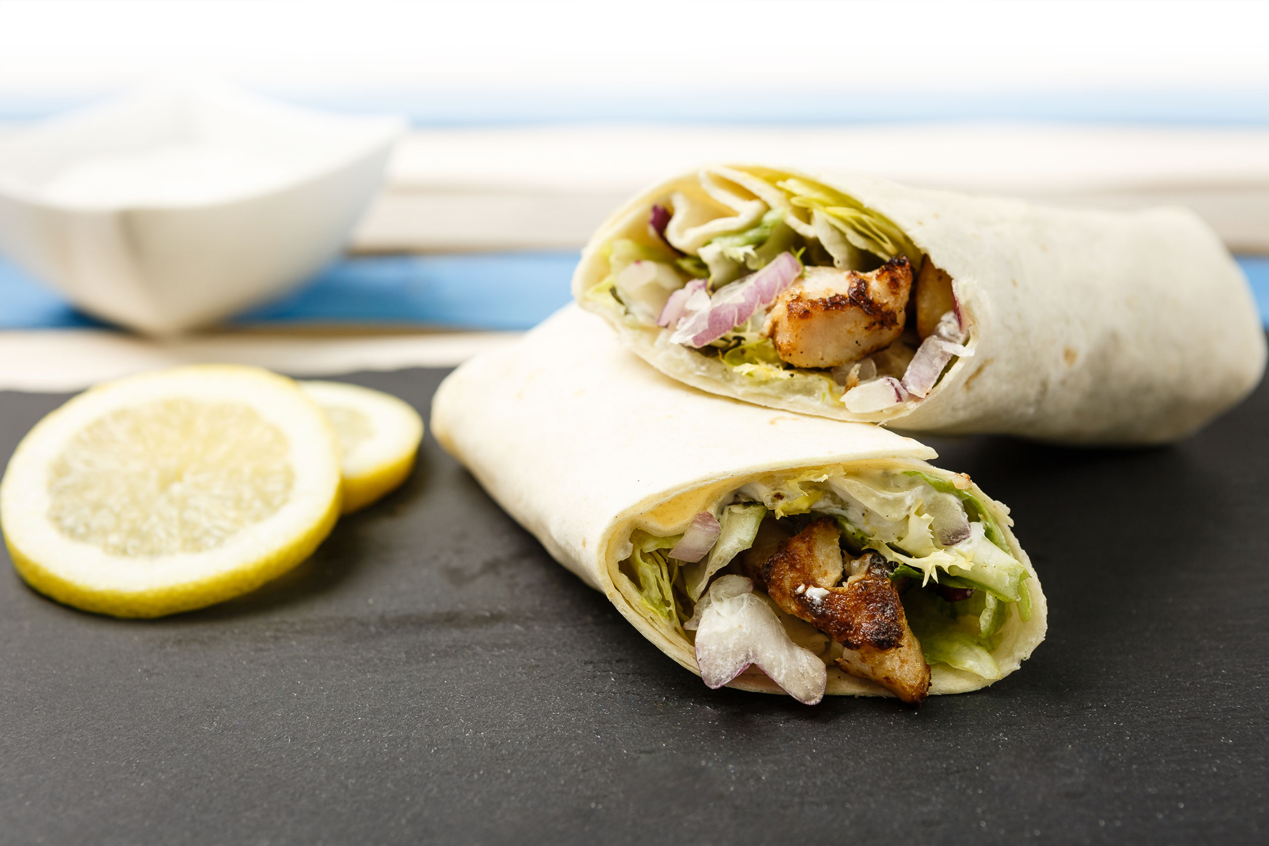 Aufeinander liegende Wraps mit Hähnchenfleisch, Zwiebeln und Salat. Daneben 2 Zitronenscheiben.